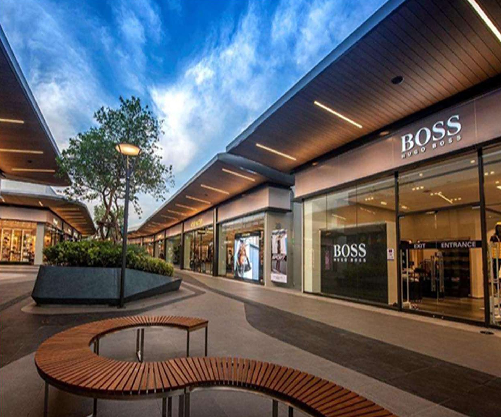 Open-air retail shopping center with covered storefronts and a curved bench
