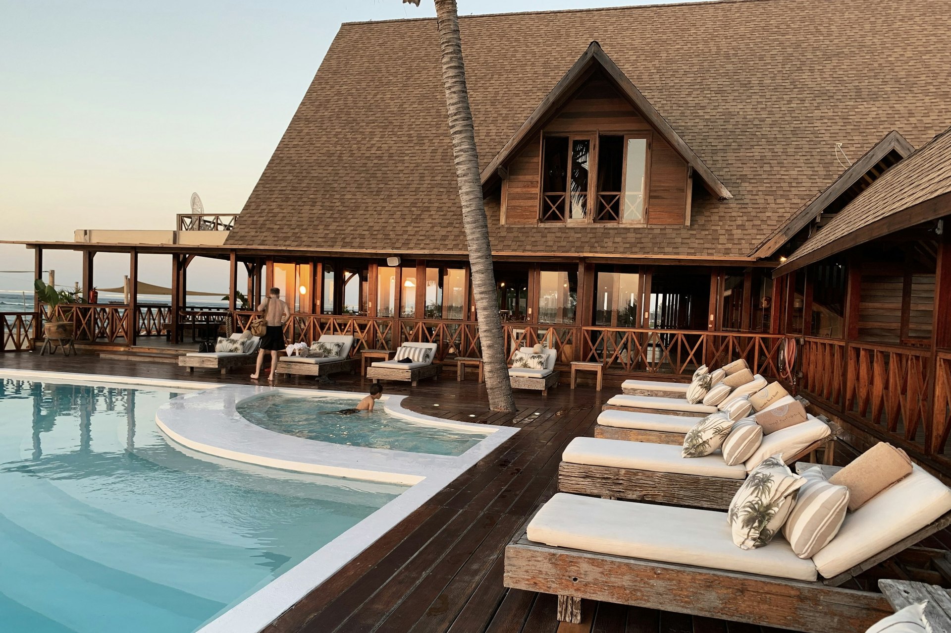 Resort hotel pool deck with lounge chairs in front of a wood lodge with a steep shingled roof