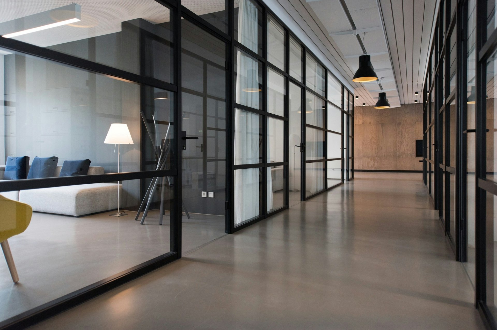 Office corridor lined with glass walled meeting rooms and pendant lights
