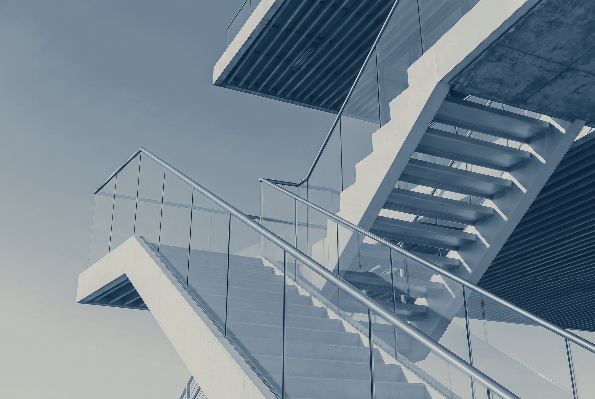 Exterior stairs with glass balustrades rising to the cantilevered floor of a modern building